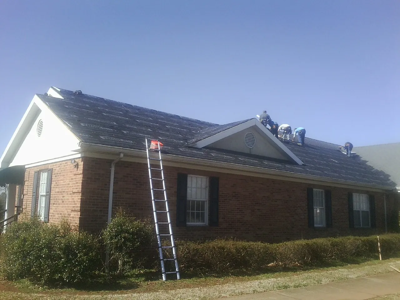 Crew tearing shingles off a brick ranch roof with a ladder set — Emergency Roof Repair work by our crew in Pomona