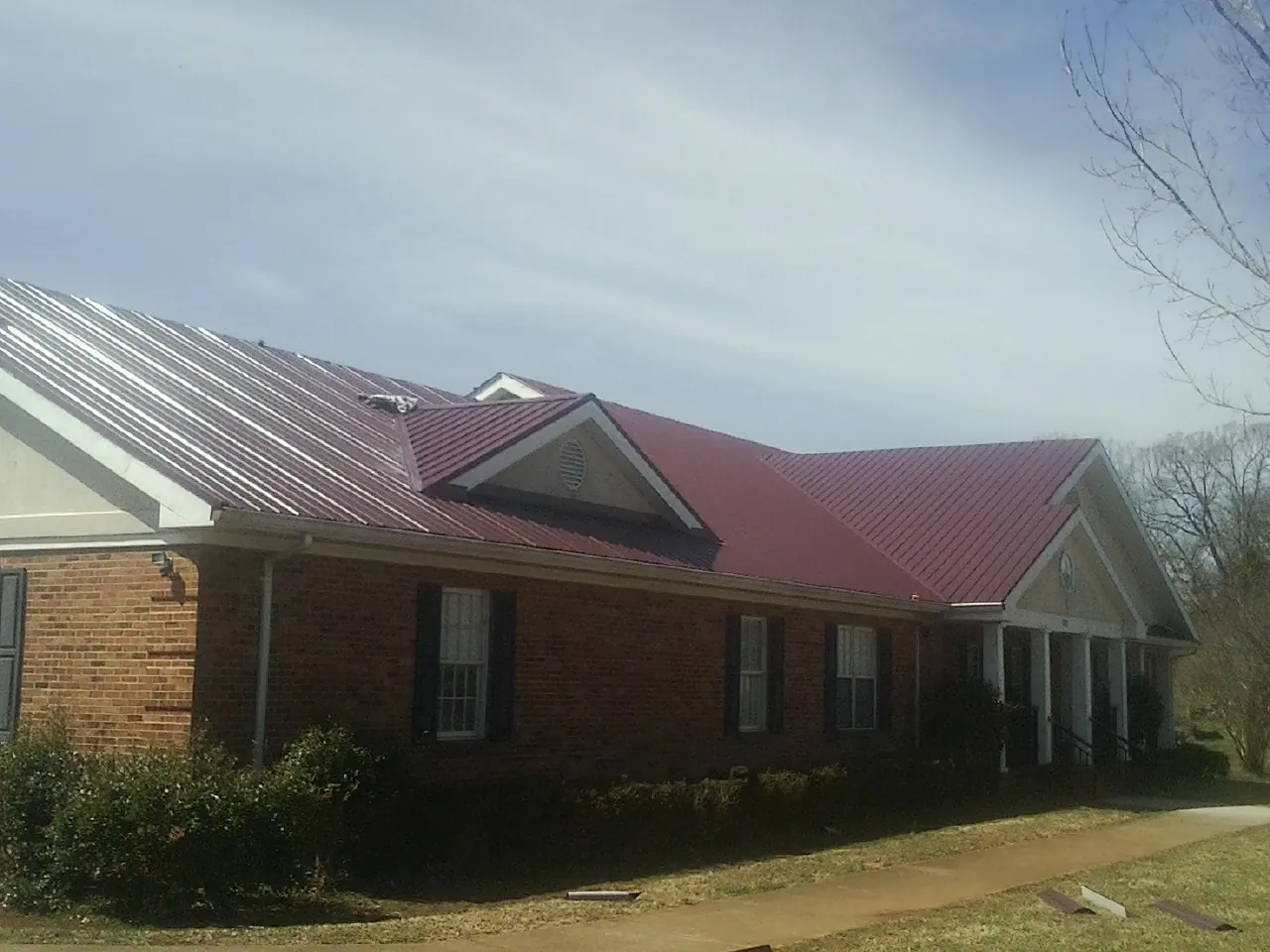 Red metal roof with gabled entries on a long brick building, from a Hail Damage Roof Repair job in Pomona